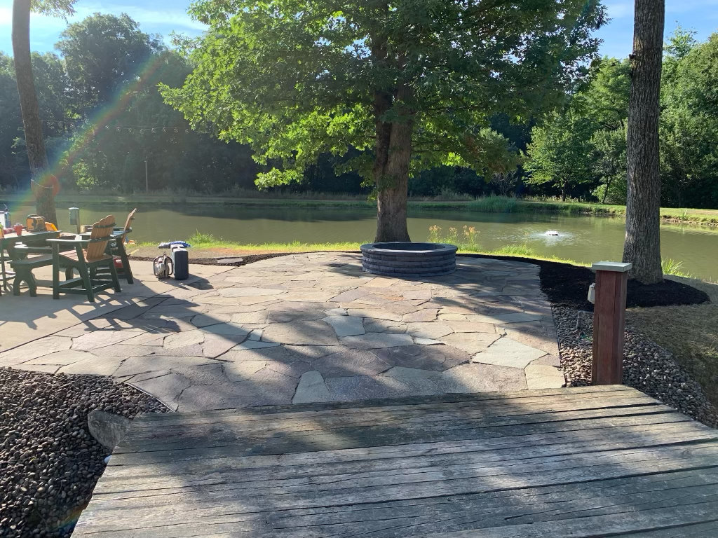 Irregular flagstone patio with Adirondack chairs and a fire pit beside a pond