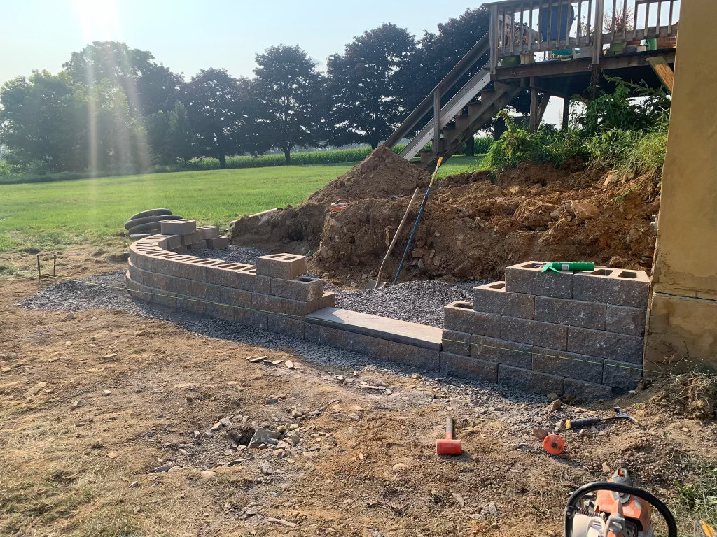 Block retaining wall under construction with pallets of block staged beside it