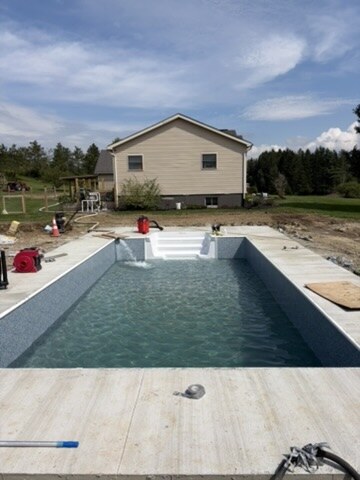 Completed 14 by 28 vinyl-liner in-ground pool filled, with white entry steps and a concrete deck