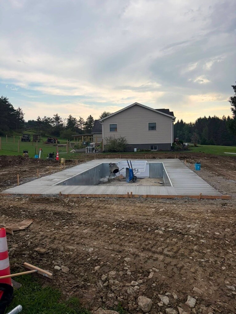 Concrete pool deck poured around a steel-wall in-ground pool at dusk, ready for the liner