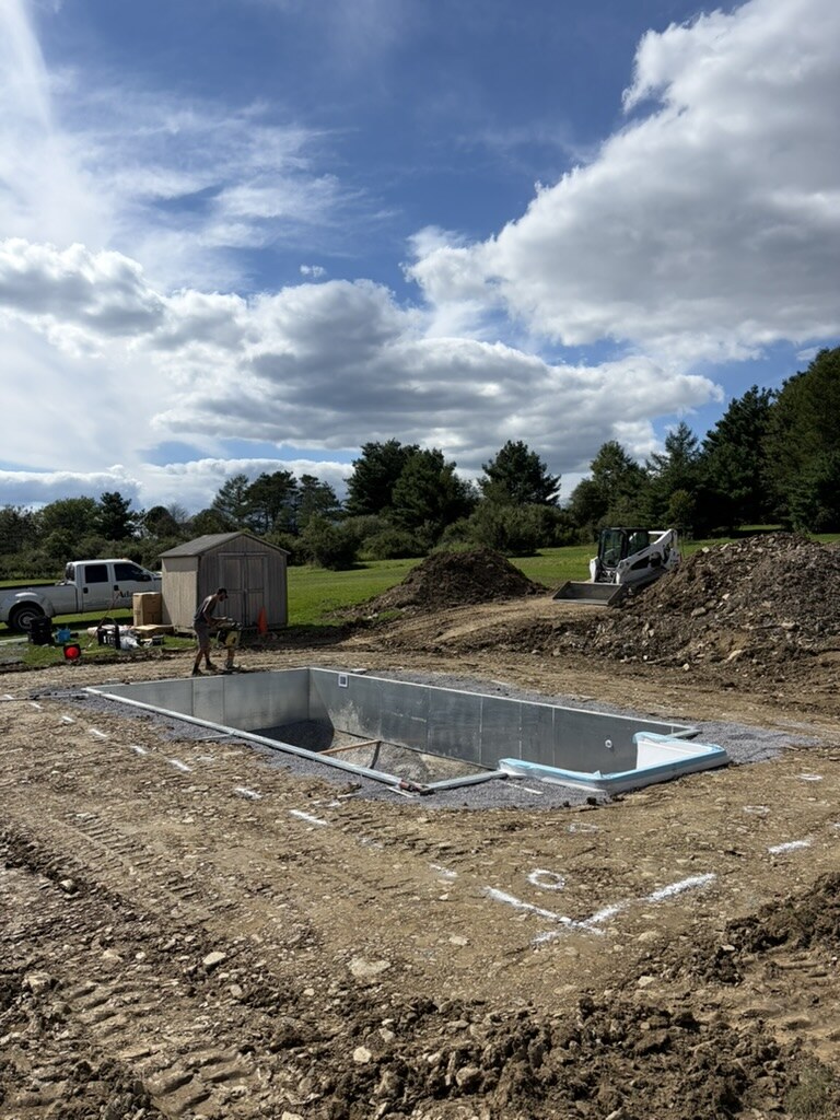 Steel wall panels and the white step unit set for an in-ground pool, skid steer on site