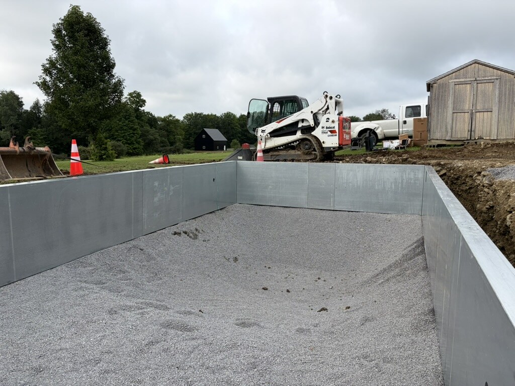 Gravel base spread inside steel in-ground pool walls with a Bobcat skid steer at the far end