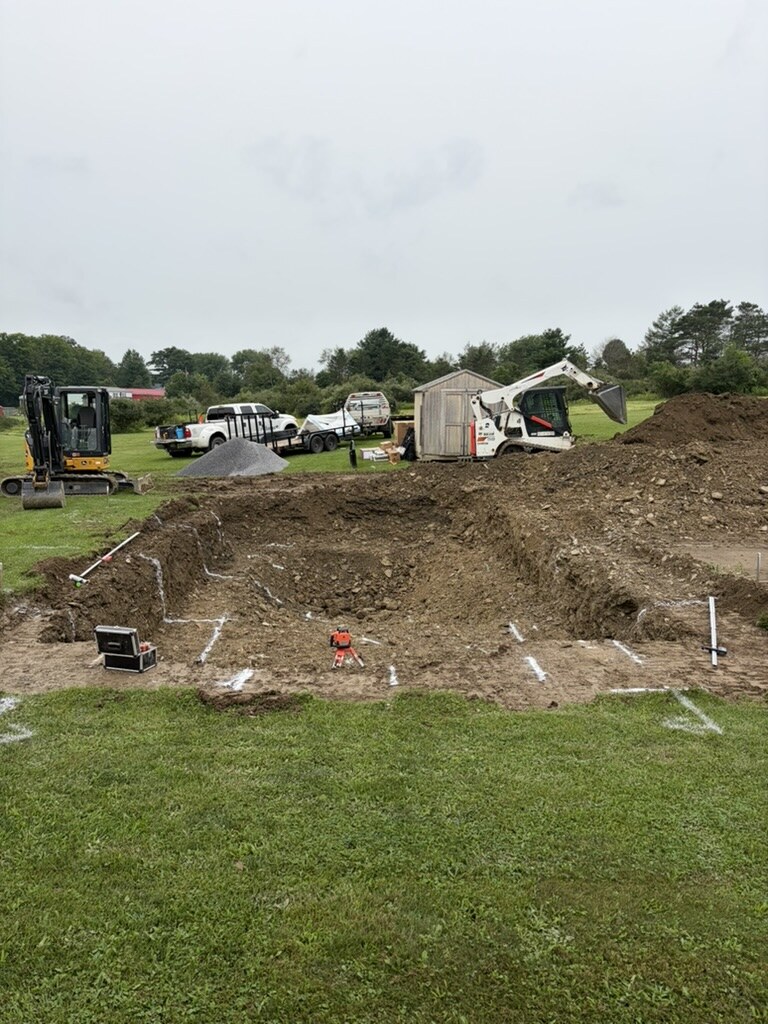 Pool excavation marked with layout paint, mini excavator and skid steer bringing in stone