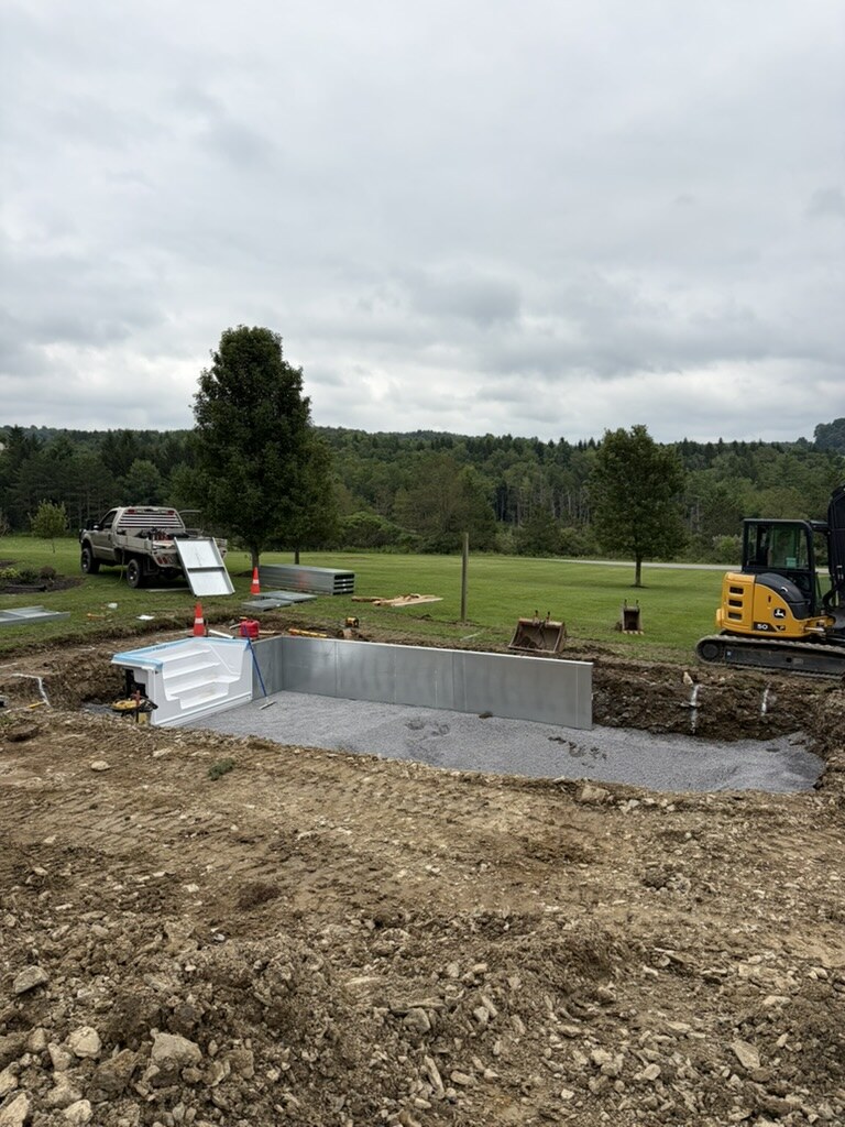 Steel pool walls and step unit standing in the excavation with the crew truck and hills behind