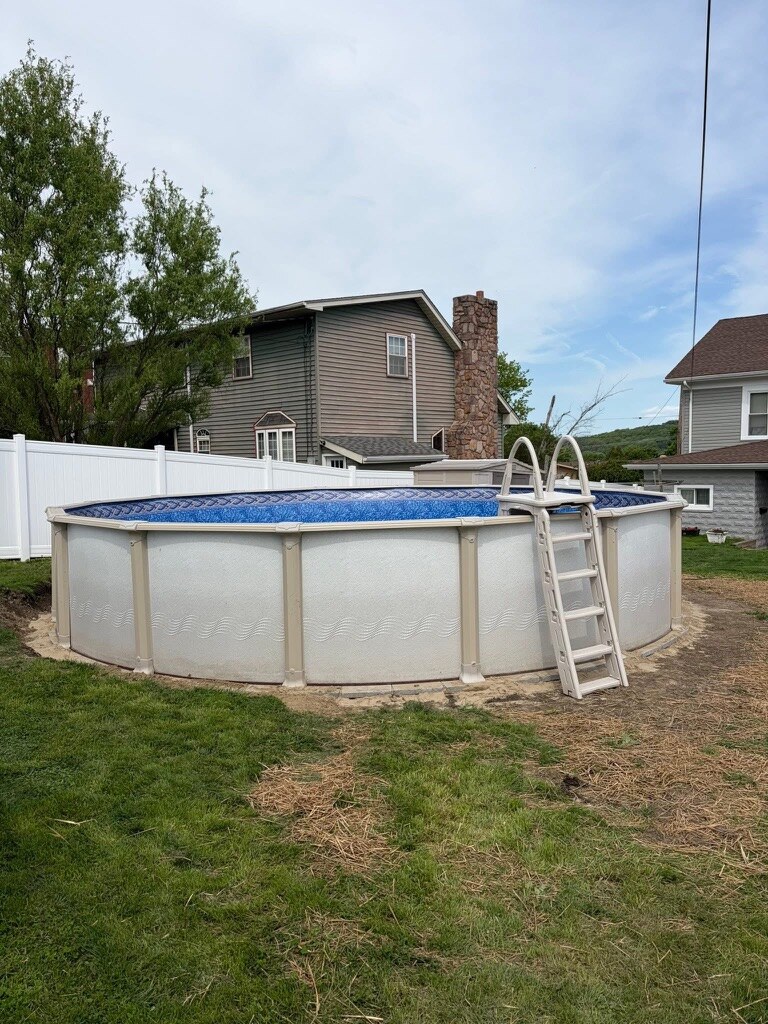Round above-ground pool with tan resin walls, blue liner and A-frame ladder beside a vinyl fence