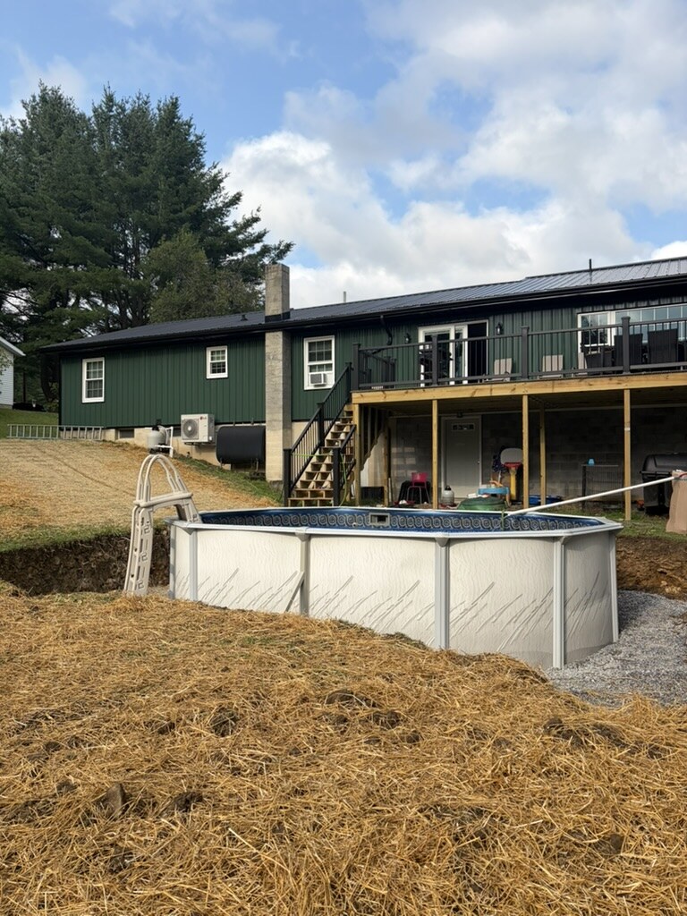 Oval above-ground pool installed below the deck of a green home, straw laid over the graded yard