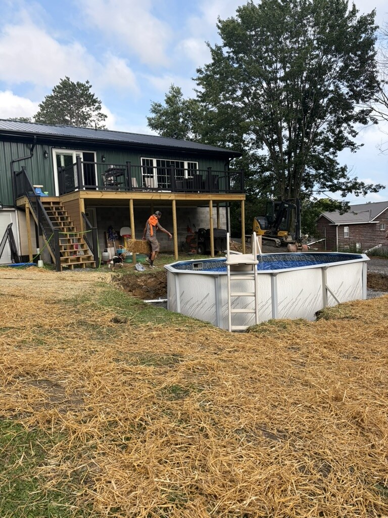 Crew finishing an oval above-ground pool install with the entry ladder set and the yard seeded