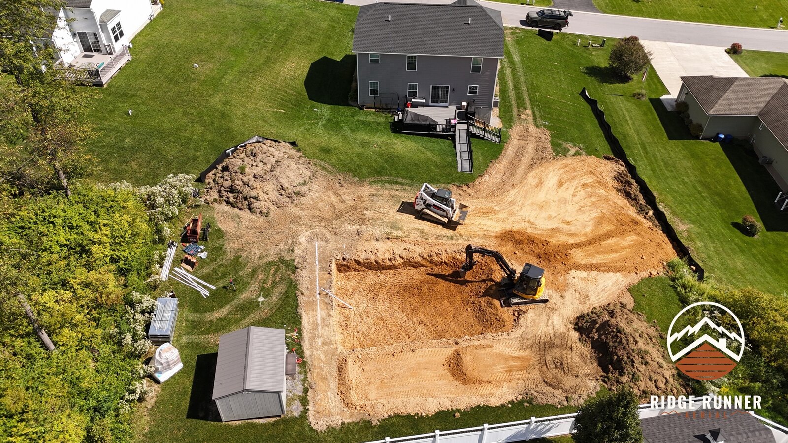 Aerial view of a new in-ground pool excavation behind a home, excavator and skid steer at work in Hollidaysburg, PA