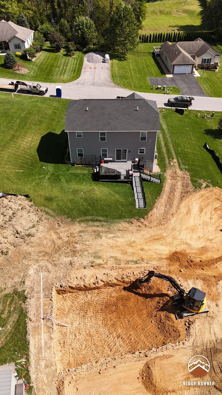 High aerial of the backyard with the pool hole squared off and the excavator in the deep end in Hollidaysburg, PA