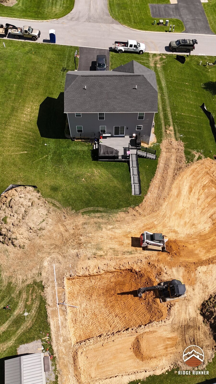Aerial of the job site from the street side, crew trucks out front and the dig behind the house in Hollidaysburg, PA