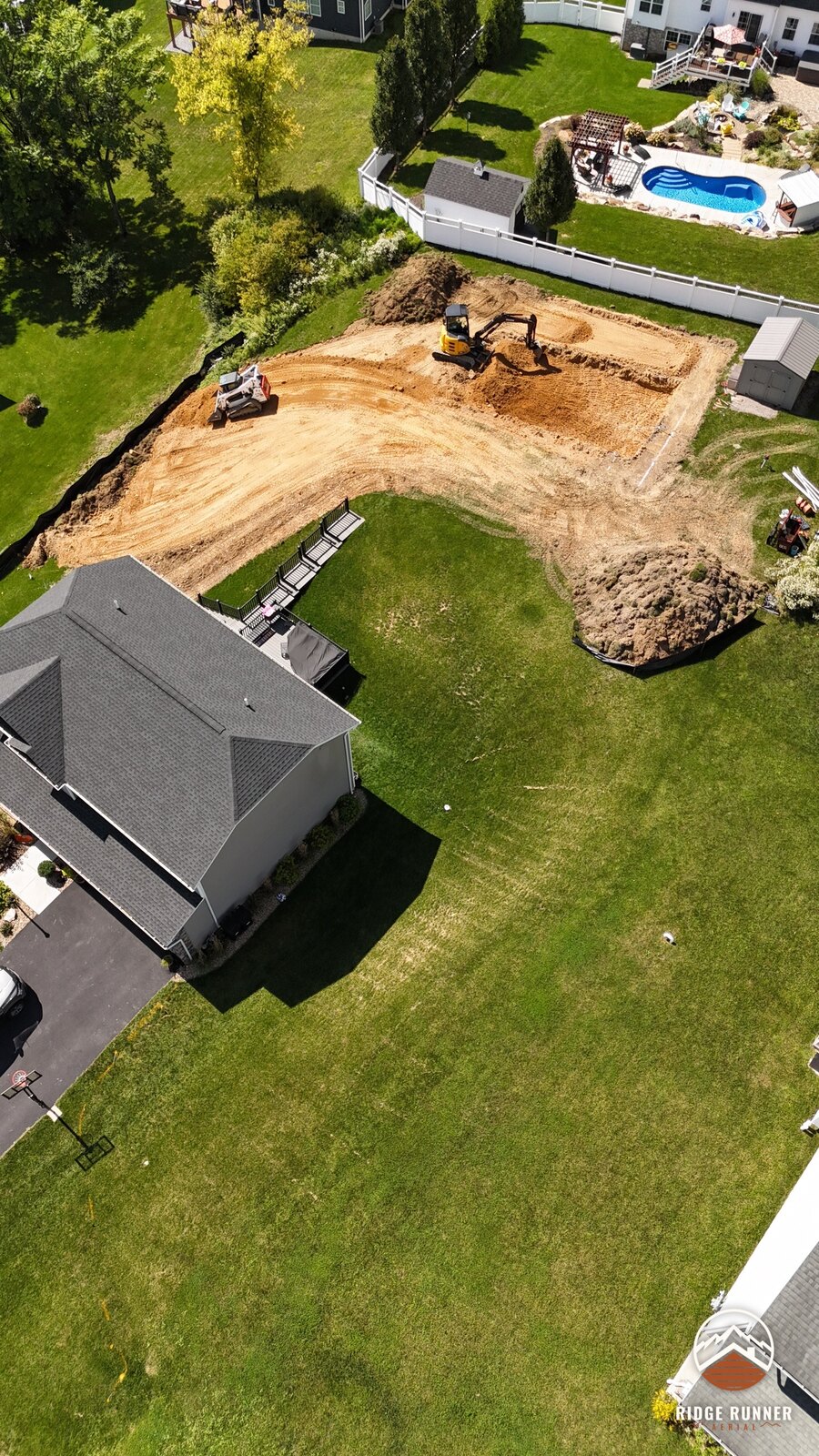 Angled aerial of the excavation with the skid steer hauling spoil past the deck stairs in Hollidaysburg, PA
