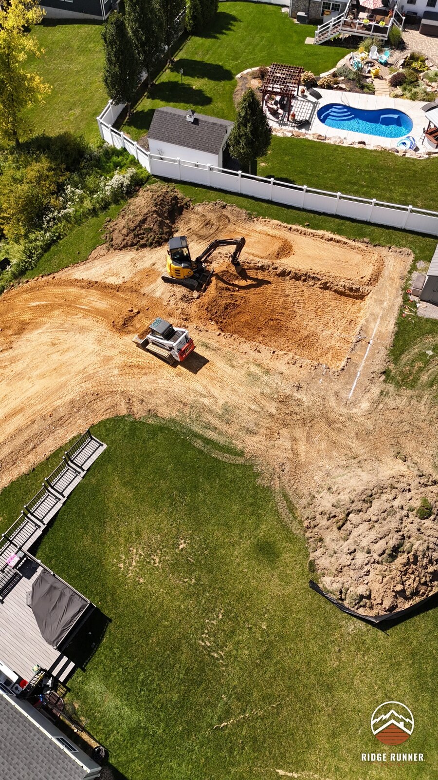 Aerial of the excavator cutting the pool floor while the skid steer runs the spoil road in Hollidaysburg, PA