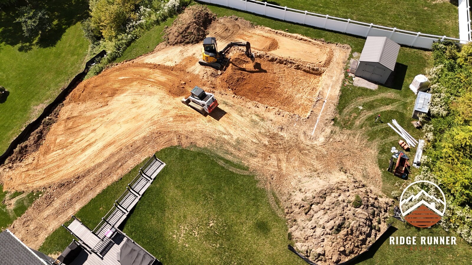 Wide aerial of the dig with the shed, silt fence and stacked pool wall panels waiting on the lawn in Hollidaysburg, PA