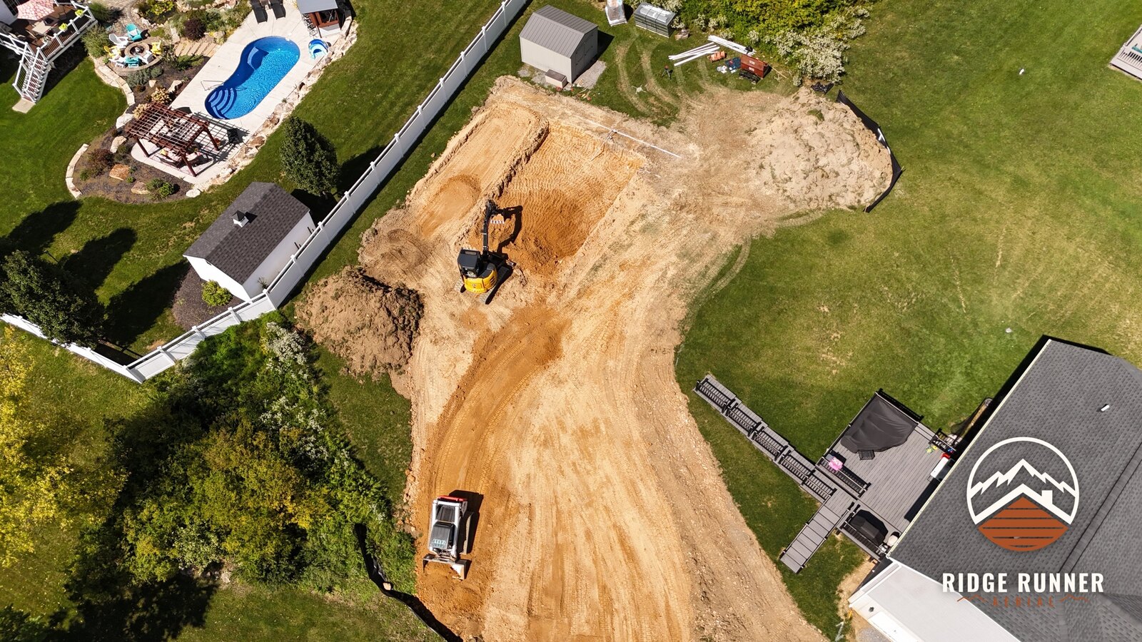 Near top-down aerial of the pool excavation and the packed access road across the yard in Hollidaysburg, PA