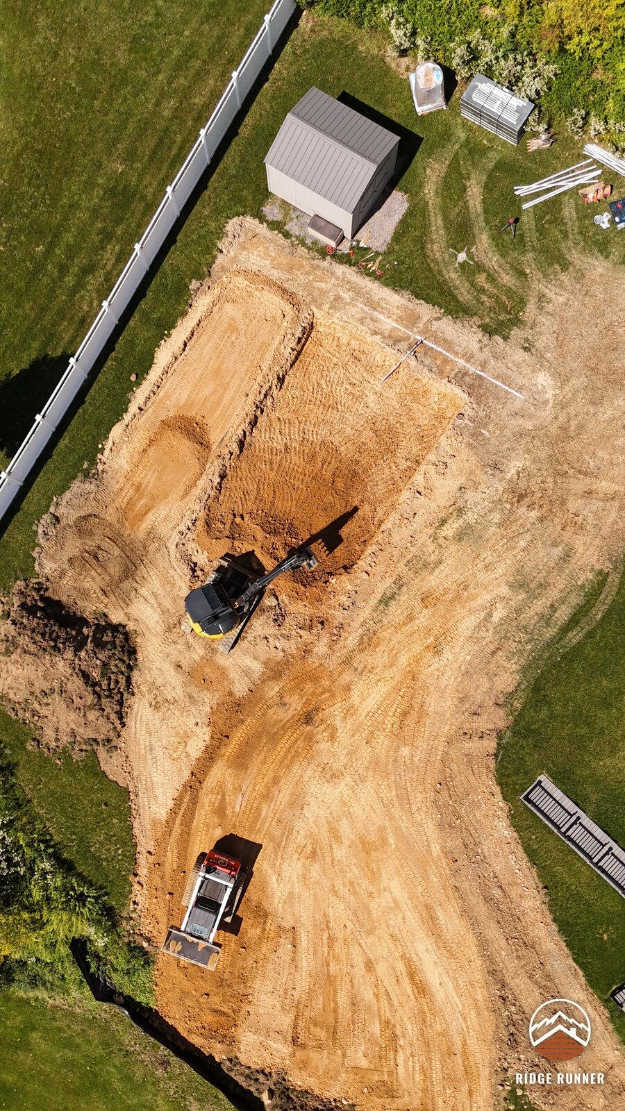 Top-down aerial of the pool dig showing the shelf for the steps and the skid steer below in Hollidaysburg, PA